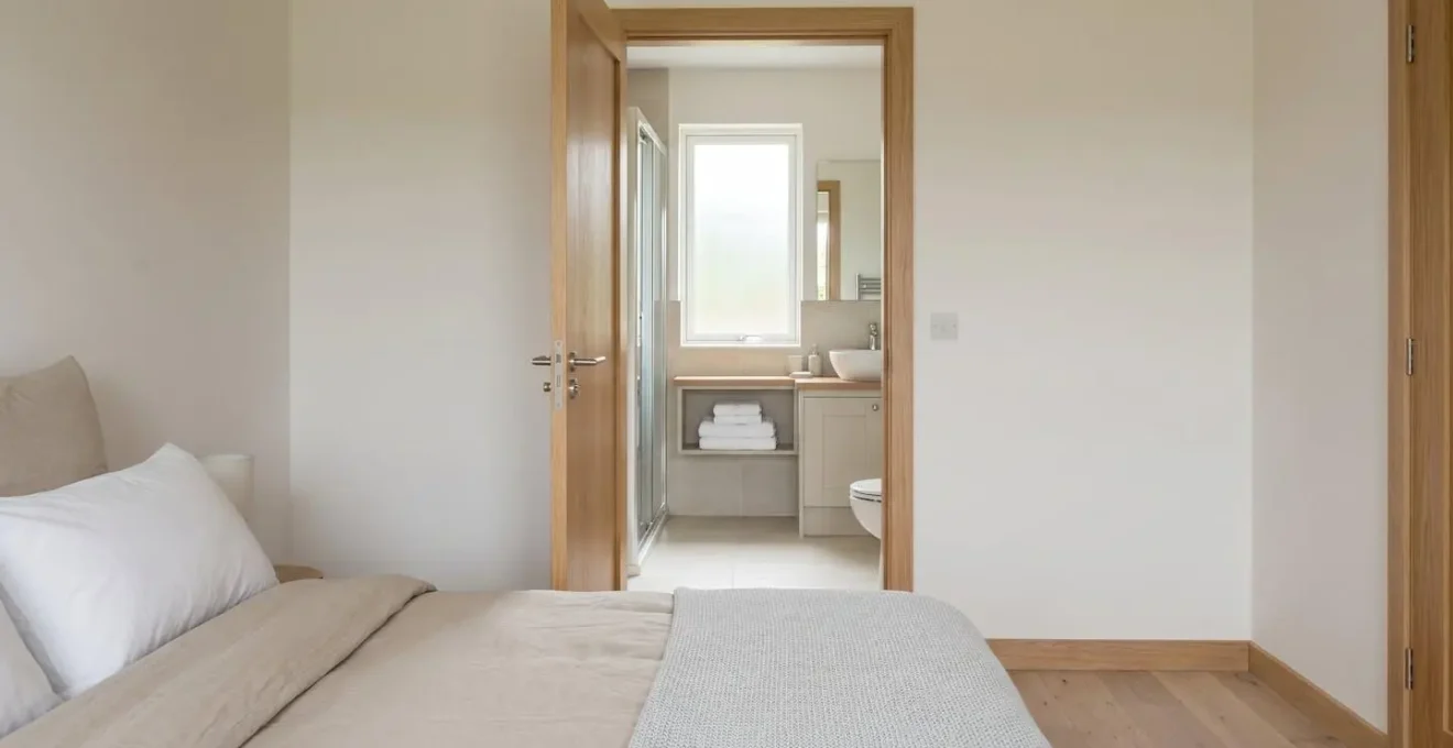 Porte ouverte entre une chambre et une salle de bains harmonisées, tons neutres et bois clair.