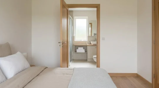 Porte ouverte entre une chambre et une salle de bains harmonisées, tons neutres et bois clair.